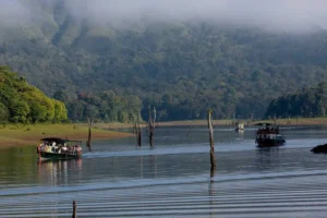 Boating on the lake at Thekkady surrounded by misty hills, showcasing Kerala hill station tourism.