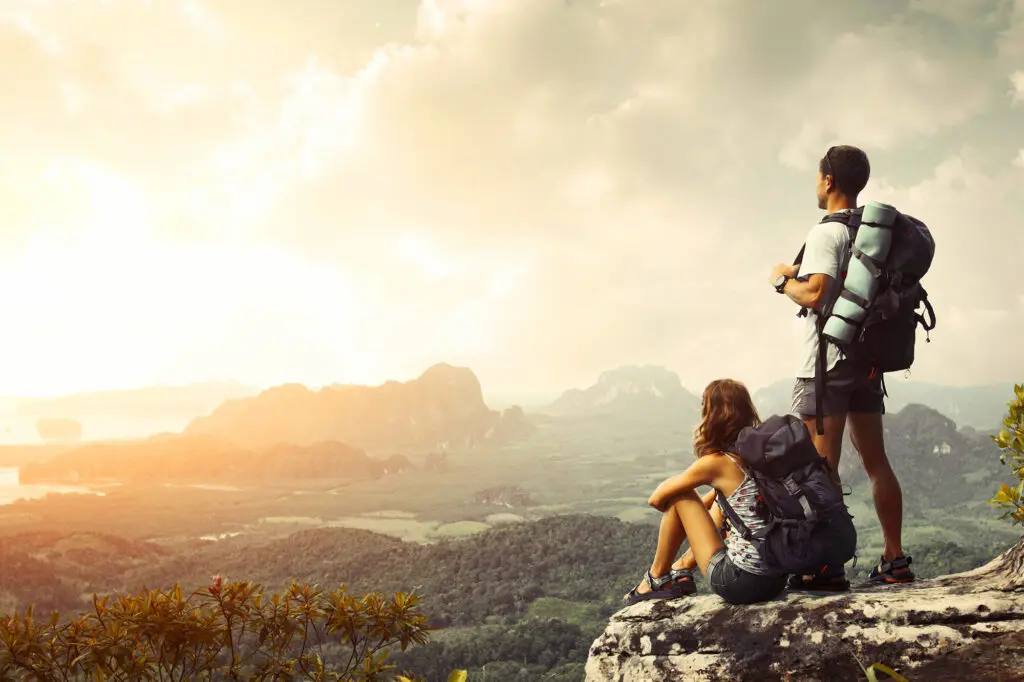 Adventurous couple relaxing on a rocky mountain overlook with panoramic valley view – Kerala travel for nature lovers